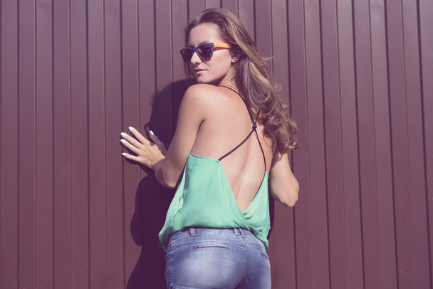 Beautiful girl in a light blouse and denim shorts, fashion stylish glasses stands on against the fence - Φωτογραφία, εικόνα