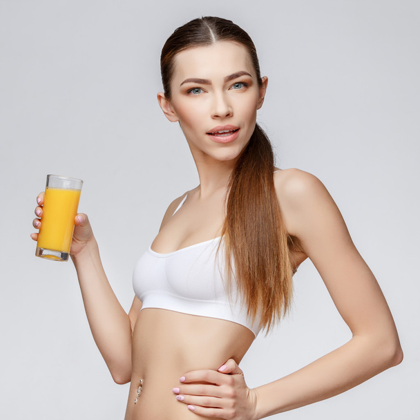 sporty woman over gray background holding glass of orange juice - Fotoğraf, Görsel