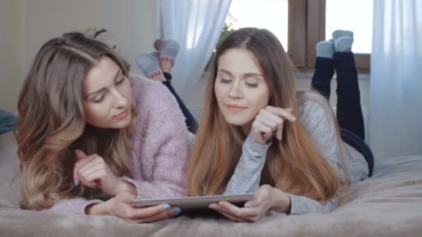 Cheerful girls lying on bed and chatting on tablet. - Video, Çekim