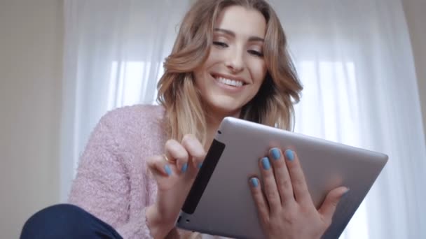 Cheerful young woman with long hair sitting on bed and using tablet computer. - Imágenes, Vídeo