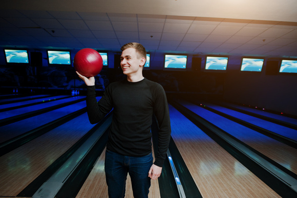 Cheerful young man holding a bowling ball standing against bowli - Foto, Bild