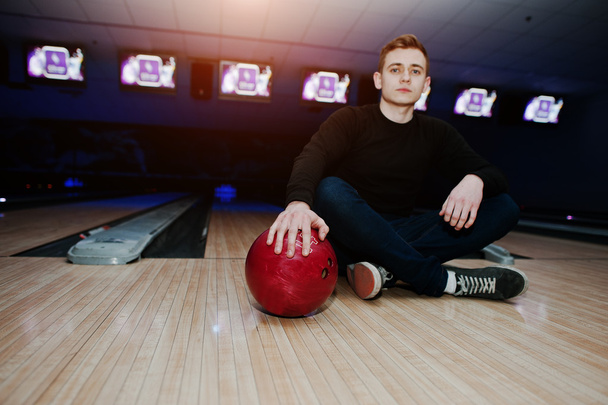 Young man holding a bowling ball sitting against bowling alleys  - 写真・画像