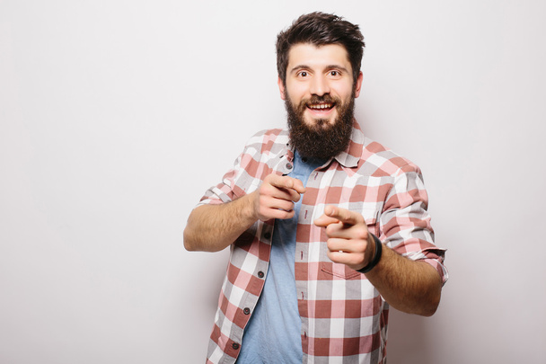 Komea nuori mies, jolla on parta, osoittaa näkymätöntä tuotteen esittelyä tai mainontaa, joka osoittaa käsillään seisoessaan valkoista taustaa vasten
 - Valokuva, kuva