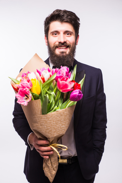 Handsome young man wearing in suit, with beard and nice bouquet of flowers against white background - Фото, зображення