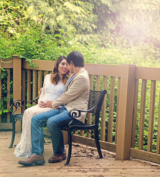 Spodziewając się mama i tata siedzi na ławce patio na świeżym powietrzu  - Zdjęcie, obraz