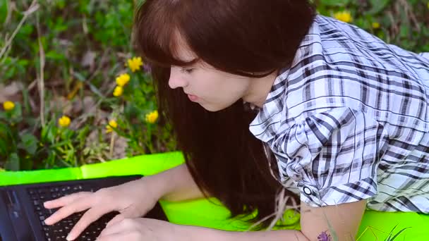 Женщина, работающая за ноутбуком, лежащим на лугу
 - Кадры, видео