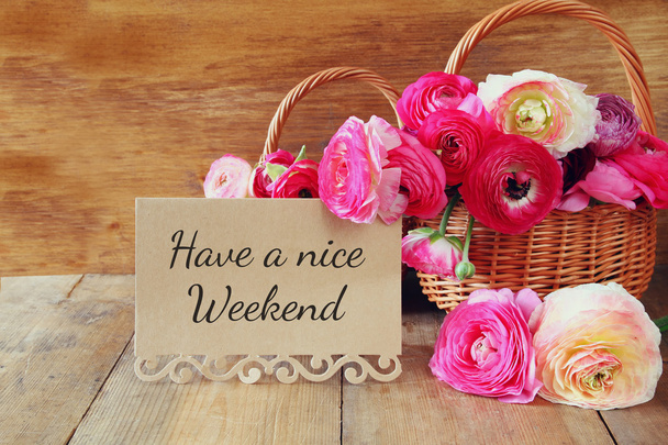 pink flowers in the basket next to card with phrase: HAVE A NICE WEEKEND, on wooden tabl - Photo, image