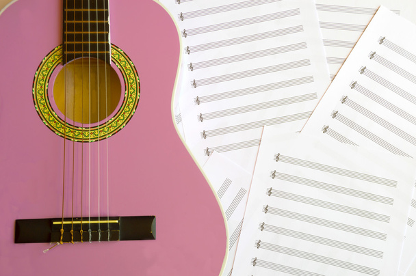 Фіолетова гітара для дітей з дерев'яною кришкою на фоні музичних листів
 - Фото, зображення