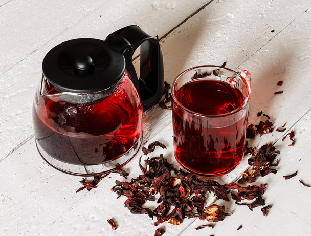 Cup of Karkadeh Red Tea with Dry Flowers and kettle on a wooden  - Fotoğraf, Görsel