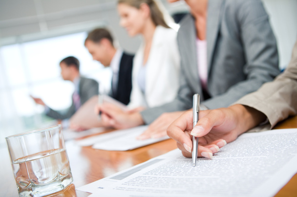 Woman's hand with pen over document on background of business group - Photo, Image