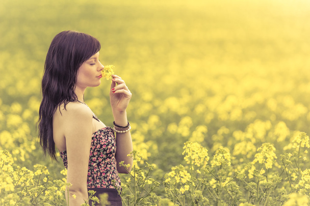 Mulher genuína no prado de flores amarelas cheirando flor
 - Foto, Imagem