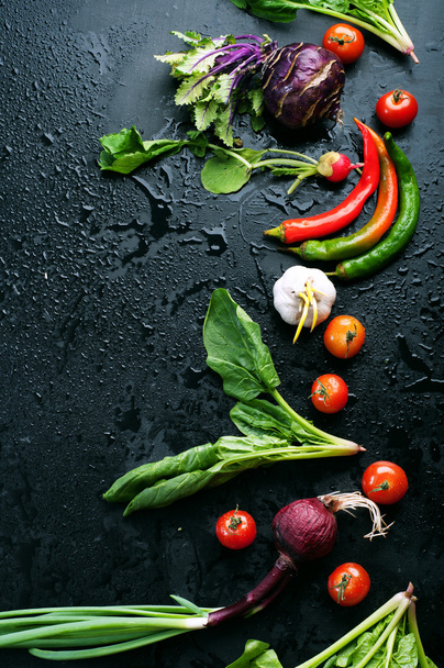 Sappige groenten en groen, zoals radijs, uien, tomaten, spinazie, peper, knoflook, kool, koolrabi en radijs op een zwarte ondergrond. Plantaardige achtergrond. Vegan concept. Plaats voor tekst - Foto, afbeelding