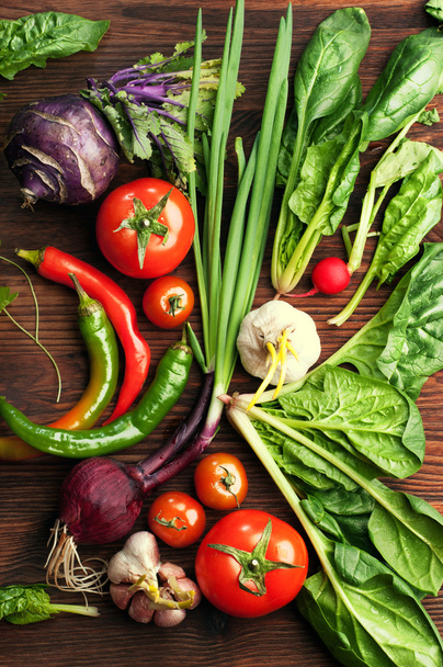 Fresh juicy vegetables and herbs, such as radishes, onion, spinach, tomatoes and hot peppers on a brown wooden board. Vegan concept. Vegetable background.  - 写真・画像
