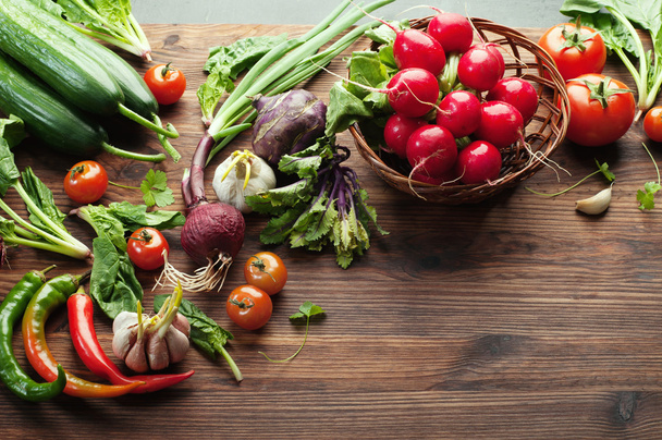 Fresh juicy vegetables and herbs, such as radishes, onion, spinach, tomatoes and hot peppers on a brown wooden board. Vegan concept. Vegetable background. Space for text - Photo, Image