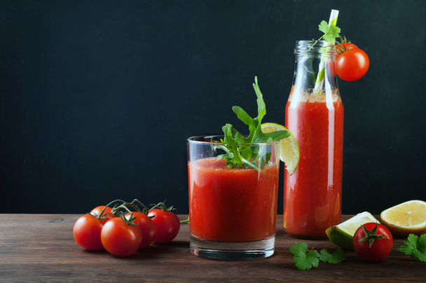 Tomato juice in a bottle and glass on a wooden board. Black background. Vegetarian concept. Non-alcoholic cocktail of tomato juice - Φωτογραφία, εικόνα