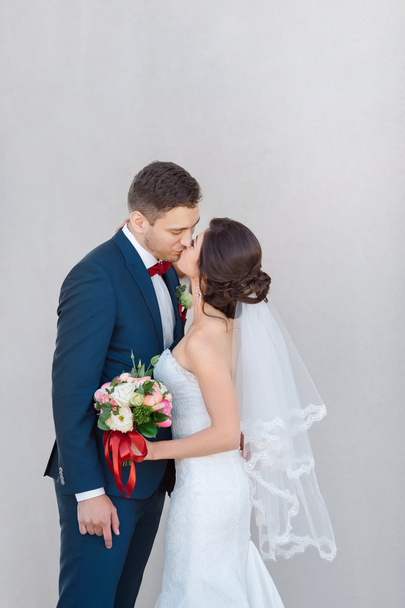 Young wedding couple kissing against a gray wall - Photo, Image