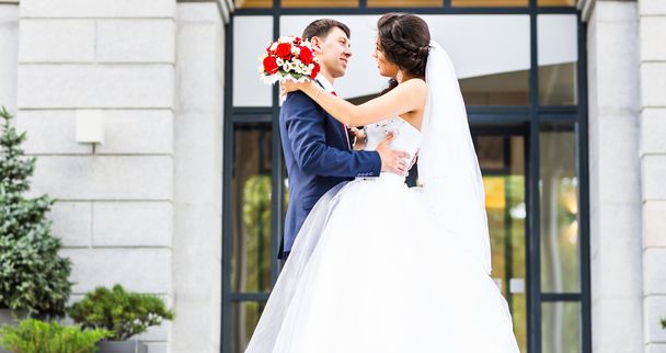 весілля пара обіймає, наречена тримає букет квітів, наречений обіймає її на відкритому повітрі
 - Фото, зображення