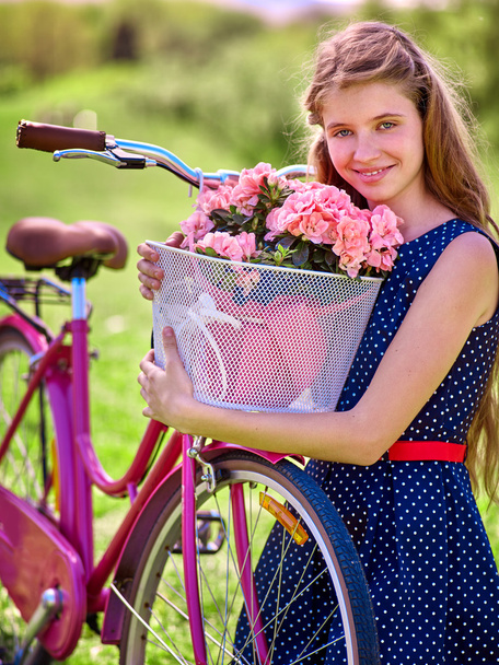 Dziewczyna ubrana w sukienkę w niebieskie groszki przejażdżki rowerowe z koszem kwiatów. - Zdjęcie, obraz