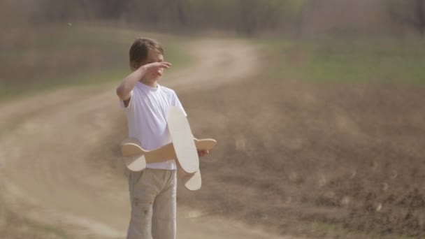 Caucasian boy playing with a model airplane. Portrait of a child with a wooden plane in a field. Boy in nature plays with the layout of the aircraft. - Imágenes, Vídeo
