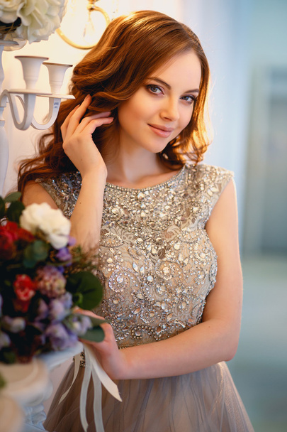 Beautiful young lady in a luxury dress in elegant interior with a bouquet of flowers - Valokuva, kuva