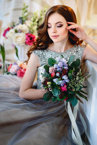 Beautiful young lady in a luxury dress in elegant interior with a bouquet of flowers - Фото, изображение
