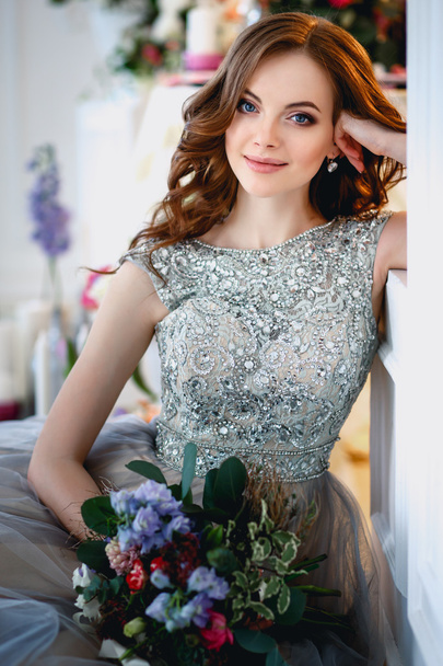 Beautiful young lady in a luxury dress in elegant interior with a bouquet of flowers - Photo, image