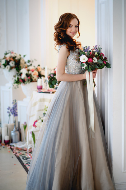 Beautiful young lady in a luxury dress in elegant interior with a bouquet of flowers - Фото, зображення