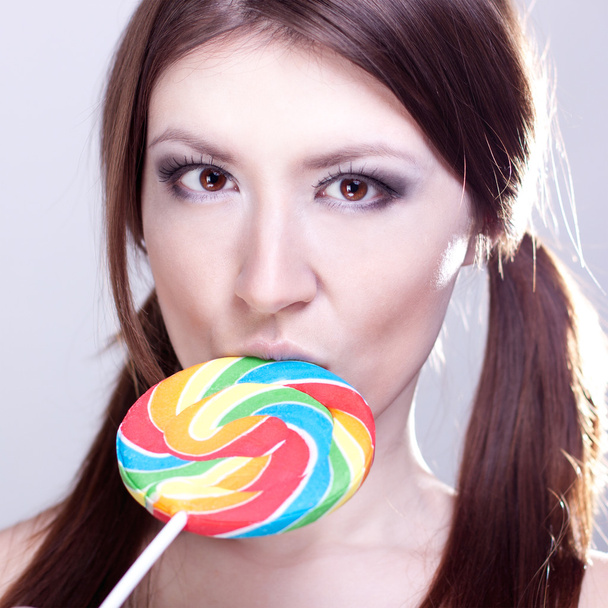 Beautiful girl with brown hair, glamorous make-up, fashion style portrait, holding candy in her hand sexy look - Zdjęcie, obraz