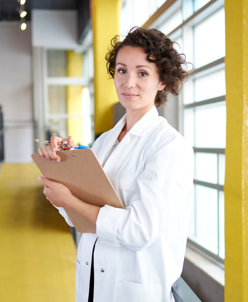 Portrait of a female doctor holding her patient chart in bright modern hospital - Photo, Image