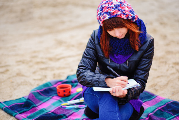 schönes Mädchen sitzt am Strand und hat Platten in einem Notizbuch - Foto, Bild