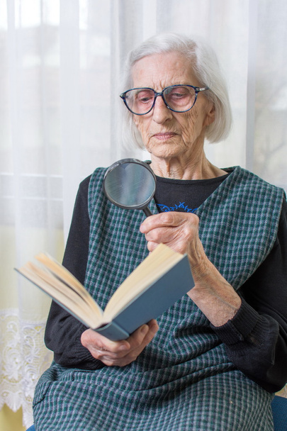 Nagymama olvasó egy könyv, nagyító segítségével - Fotó, kép
