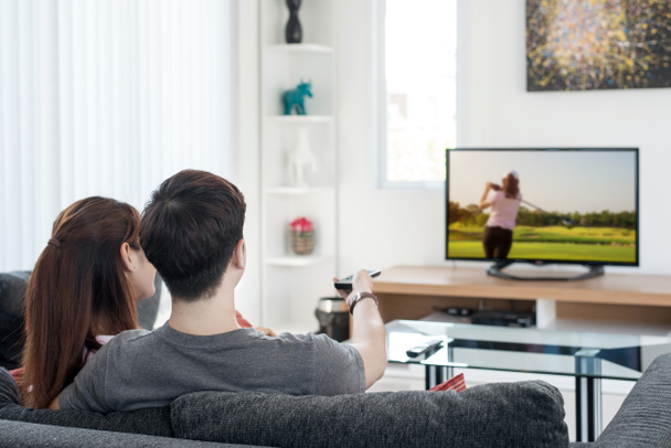 若いアジアのカップル ゴルフ スポーツを見るテレビで自宅 - 写真・画像