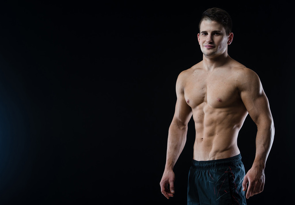 junges und fittes männliches Model posiert mit seinen Muskeln und blickt direkt in die Kamera - Foto, Bild