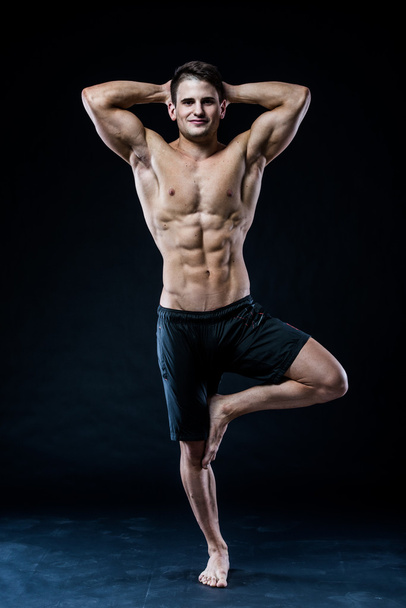 Hombre muscular balanceándose en la sensación de una pierna relajado fondo oscuro
 - Foto, imagen