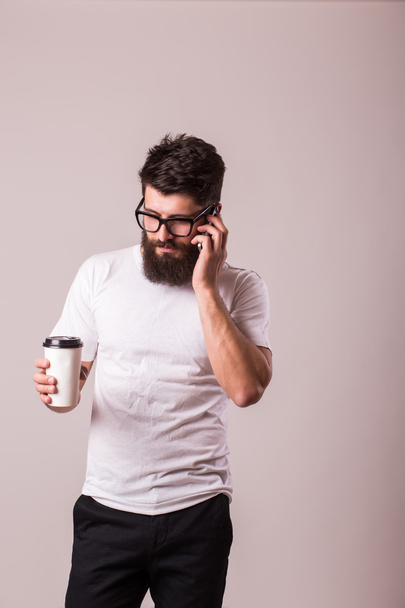 Γενειοφόρος νεαρός άνδρας με καφέ στο χέρι ματιά στην κάμερα  - Φωτογραφία, εικόνα