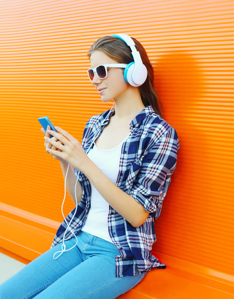 Woman in headphones listens to music using smartphone over color - Foto, afbeelding