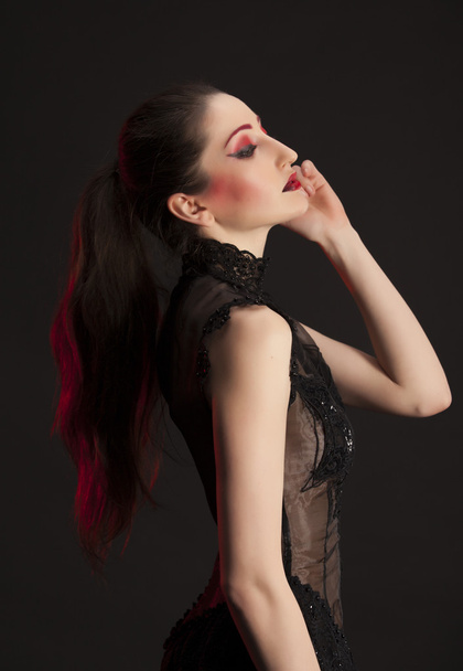 Portrait of beautiful young brunette woman in black dress against dark background, highlighted with red - Foto, afbeelding