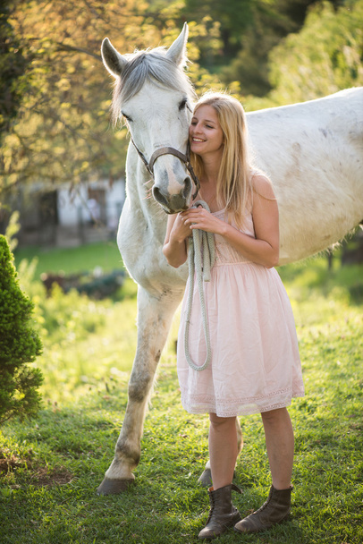 Mladá blondýnka pózuje venkovní s bílým koněm.  - Fotografie, Obrázek