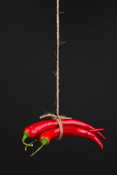 Red hot chili peppers tied with rope isolated on black - Foto, imagen