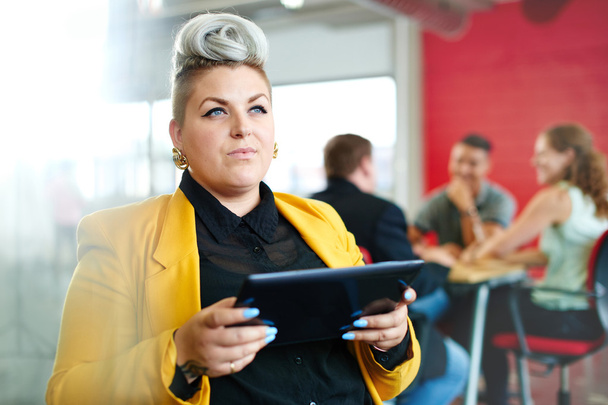 Designer féminin confiant et énergique travaillant sur une tablette numérique dans un espace de bureau créatif rouge
 - Photo, image