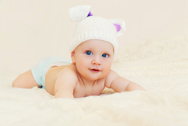 Cute baby in knitted hat with rabbit ears crawls on bed home - Foto, Imagem