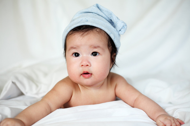 Słodki noworodka w niebieskim pomponem kapelusz leży na łóżku - Zdjęcie, obraz