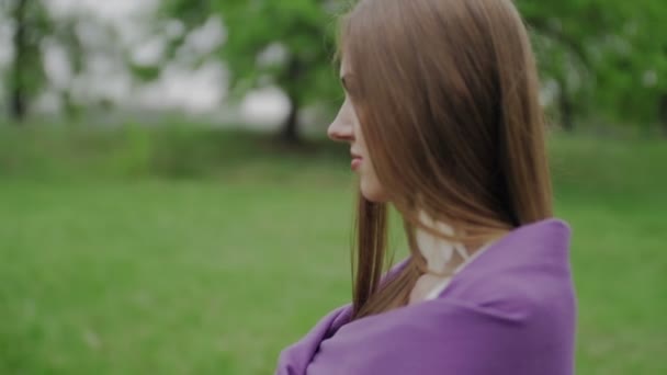 Piękna dziewczyna w fioletowy peleryna stoi w parku - Materiał filmowy, wideo
