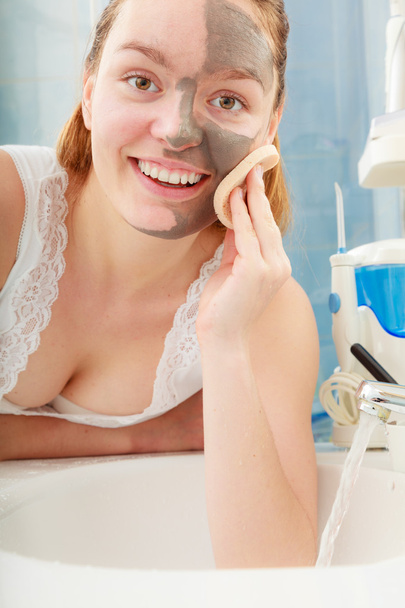 woman removing facial clay mud mask in bathroom - Photo, image
