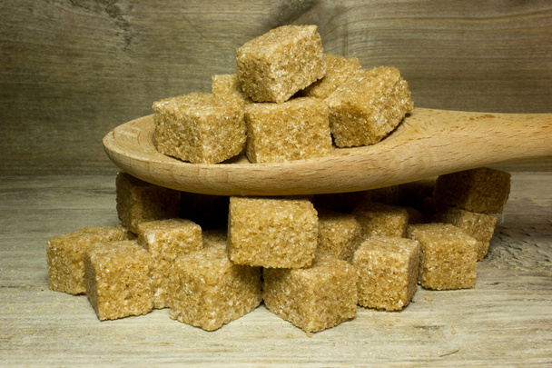 Кубики коричневий тростинний цукор і ложка на дерев'яному фоні
 - Фото, зображення