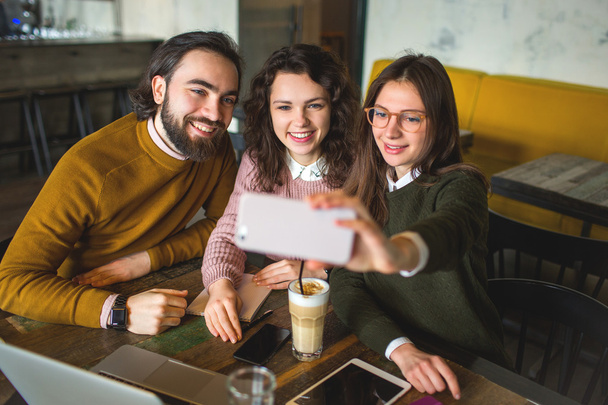 Three happy young friends taking selfie with smartphone in cafe - Photo, Image