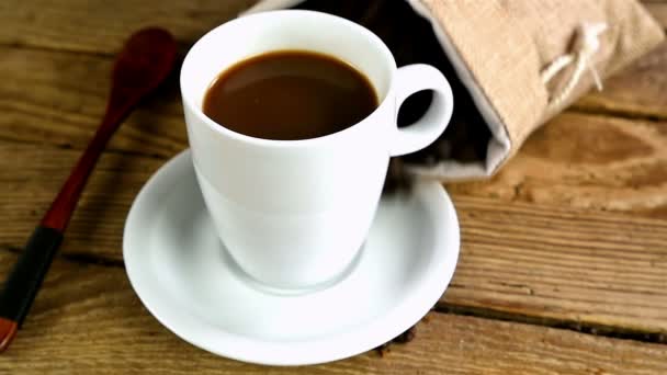 Tas met koffie bonen falls en koffiebonen zijn verspreid over de kop met koffie, slow-motion - Video