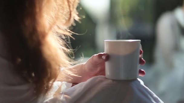 Girl sits in a white coat in bed with a coffee - Materiał filmowy, wideo