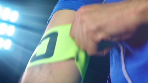 Voetbal, voetbalspel. Professionele voetballer in blauwe outfit zetten kapitein tape, zwarte achtergrond - Video