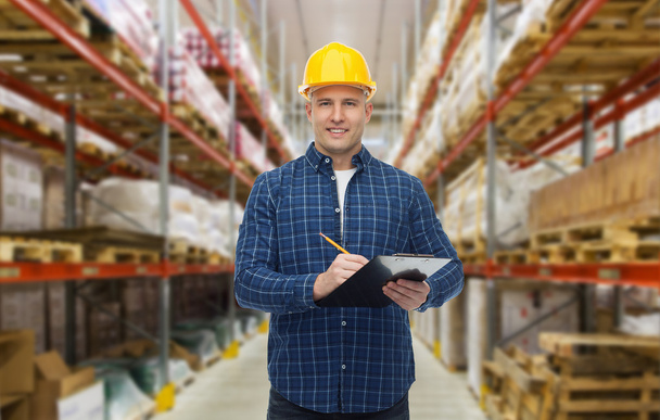 happy man in helmet with clipboard at warehouse - Photo, image